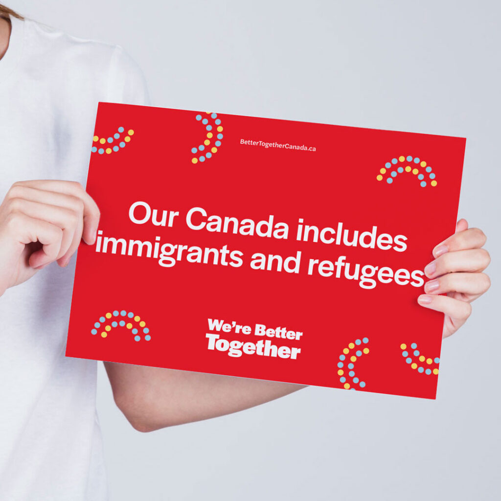 A handheld sign that reads "Our Canada includes immigrants and refugees."